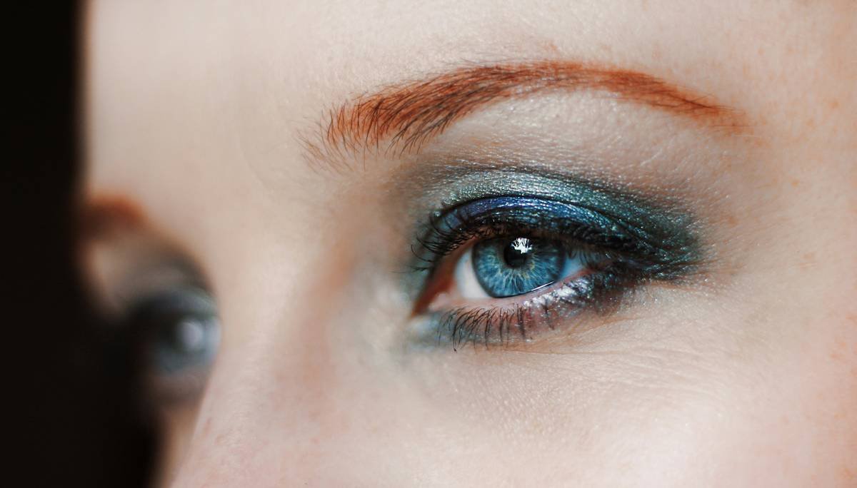 Actor applying dramatic theater makeup with precision brushes under stage lighting